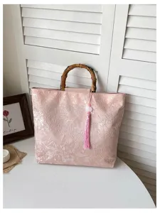 Détail de la pochette rose avec poignée en bambou, motif floral et charm gland.