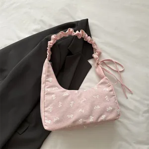 Close-up detail of a pink gingham shoulder bag with white bow embroidery and pleated handle.
