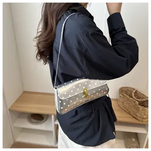 Detail shot of the silver polka dot shoulder bag with gold lock worn on body in indoor scene.