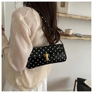 Detailed view of the black and white polka dot patent leather shoulder baguette bag, stylish.