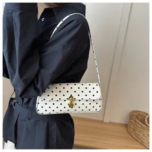 Close-up detail of white polka dot shoulder underarm bag with gold clasp in daily commuting scene.