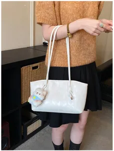 Detailed shot of white PU leather shoulder bag with cute bear charm and thin straps, indoor view.