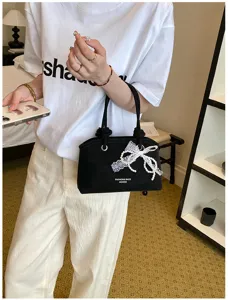 Detailansicht der eleganten schwarzen Handtasche mit weißer Spitzen Schleife und Perlen.