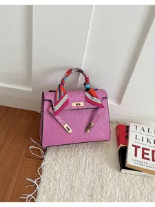 Bolso de mano rosa con textura avestruz, elegante bolso bandolera de mujer con detalle de pañuelo.