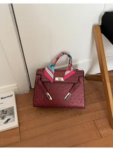 Detalle del bolso de cuero burdeos con estampado de avestruz y pañuelo de seda colorido.