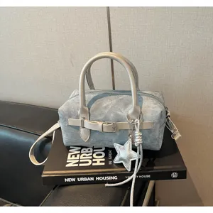 Detailed view of the light blue denim pillow shoulder bag with star charm and front belt.