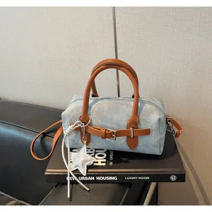 Detail view of a stylish denim pillow bag with brown leather handles and star charm.