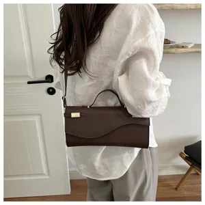 Detailopname van de vintage donkerbruine PU lederen schoudertas met gebogen flap en handgreep.