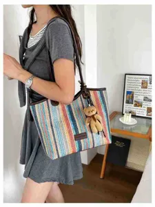 Detail view of the colorful woven tote bag featuring a cute bear pendant and leather handles.