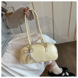 Close up detail view of elegant light yellow shoulder pillow bag featuring pearl bow pendant.