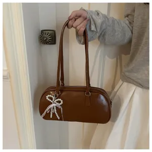 Brown shoulder pillow bag detail shot showcasing exquisite pearl lace bow pendant and fine handles.