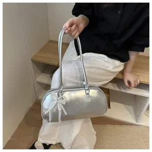 Detail shot of stylish silver metallic shoulder pillow bag featuring elegant pearl bow pendant.
