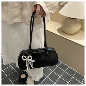 Detail view of black patent leather shoulder bag with elegant pearl bow pendant decoration.