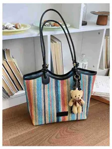Colorful striped straw tote bag featuring black leather handles and cute teddy bear plush pendant.