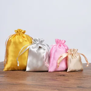 Four colorful satin drawstring pouches in different sizes on a wooden surface
