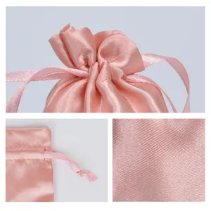 Macro view showing the smooth pink satin fabric texture and drawstring detail on a luxury pouch