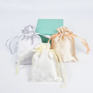 Three satin drawstring pouches in white, gray, and gold next to a blue gift box