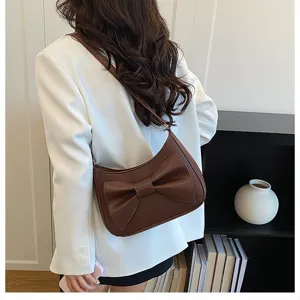 Detail shot of a brown underarm shoulder bag with a stylish bow design in a chic room setting.