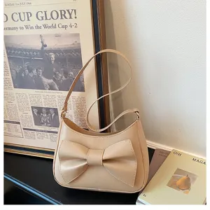 Detail view of the elegant beige shoulder bag featuring a stylish front bow and smooth finish.
