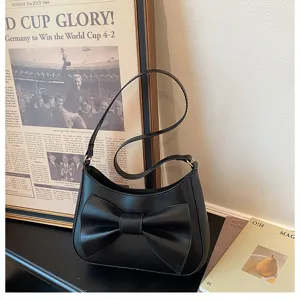 Detail shot of a black shoulder bag featuring a stylish front bow on a dark surface.