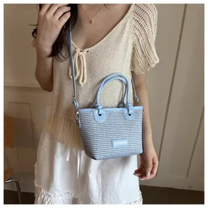 Detailed shot of a light blue woven bucket bag with knot handles and crossbody strap.