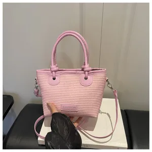 Pink woven bucket bag with knot handle and crossbody strap, fashionable beach style detail view.