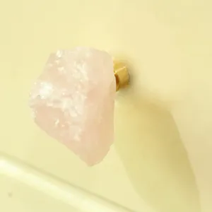 Gros plan détail du bouton de meuble en quartz rose brut, poignée de tiroir en laiton.