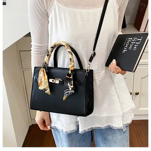 Detailed view of black leather handbag with chic printed scarf handle and gold hardware.