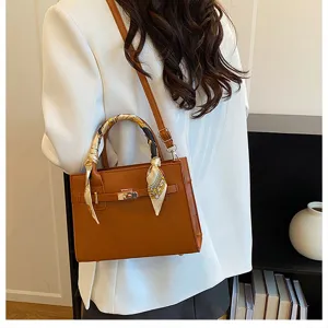 Detailed view of brown women's structured handbag with decorative silk scarf and metal lock.