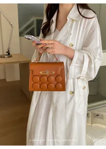 Detailed shot of trendy brown leather handbag with unique round button decor and chic clasp.