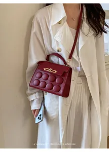 Red women's handbag with round padded design, gold metal clasp, and shoulder strap.