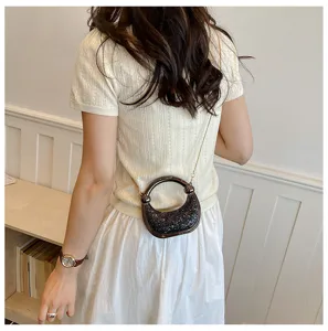 Detailed view of a trendy sparkly crescent shoulder bag with a round handle and gold chain strap.