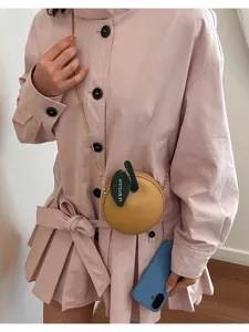 Close-up detail of chic round fruit crossbody bag with chain strap and leaf tag accent.
