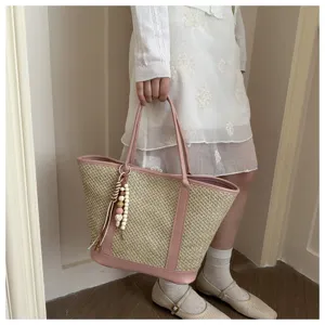 Detailopname van een zomerse strooien tote tas met roze leren afwerking en houten kralen hangertje.