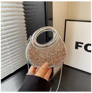 Detailed shot of glittering crescent evening bag with silver acrylic handle and chain strap.