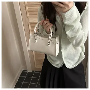 Detail view of white leather mini motorcycle pillow handbag with metal studs and top handle.