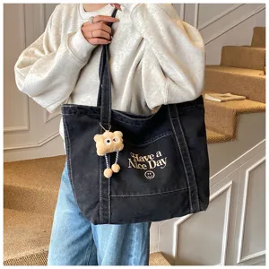 Detailopname van een zwarte denim shopper tas met witte stiksels en leuke tekstprint.