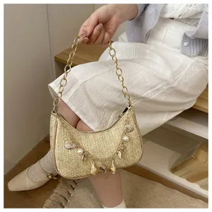 Detail view of straw woven shoulder bag with pearl shell charms and metal chain strap.