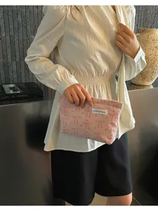 Gros plan d'une pochette rayée à motif de nœud, présentée par un mannequin en intérieur.