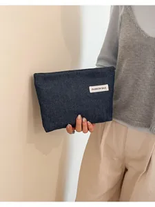 Gros plan d'une pochette en denim élégante tenue à la main, montrant la texture et l'étiquette.