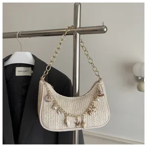 Woven underarm bag detail featuring straw texture, golden chain strap, and shell pearl charms.