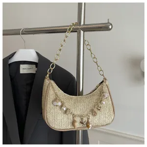 Detailed view of trendy straw woven underarm bag with gold chain and pearl shell charms.