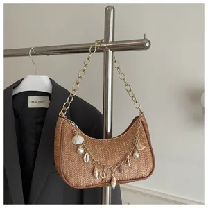 Chic woven straw underarm shoulder bag featuring golden chain strap and decorative seashells.