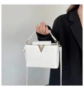 Élégant sac à bandoulière blanc pour femme avec fermoir métallique doré en V et poignée supérieure.