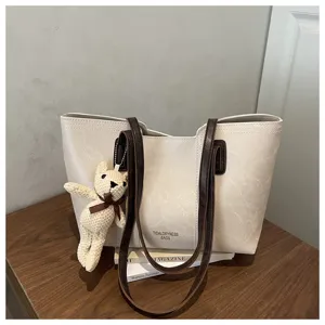 Dettaglio della borsa shopper bianca con manici marroni e grazioso ciondolo orsetto in maglia.
