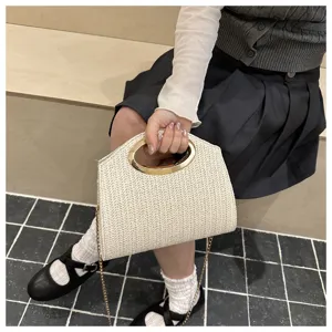 Dettaglio della borsa a tracolla chic in paglia intrecciata con manico in metallo dorato.