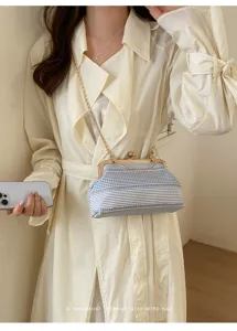 Close-up detail of blue and white striped fabric kiss-lock handbag with gold chain strap.
