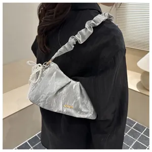 Detailed view of silver pleated underarm cloud bag with pearl lace pendant and chic metal logo.