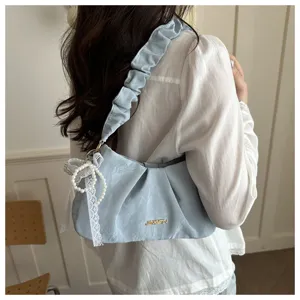 Detail shot of a light blue pleated underarm bag featuring a delicate pearl lace pendant and ruffle strap.