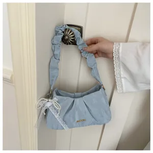 Detail view of a light blue ruched shoulder bag featuring a dainty pearl lace pendant and chic handle.